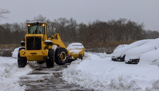 Snowplow plowing parking lot with cars in it