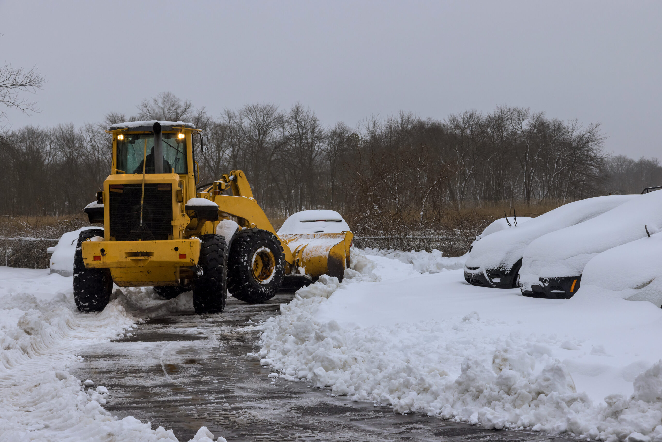 Snowplow plowing parking lot with cars in it