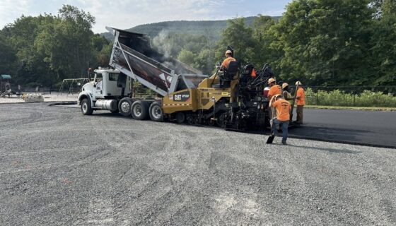 Men paving a road with a dumpster truck and paving machine